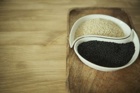 White sesame and black sesame seeds on a white plate. Wooden table. Soft selective blurred background.の写真素材