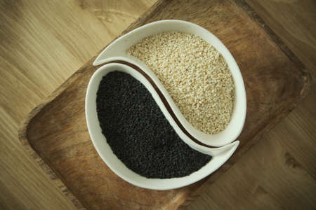 White sesame and black sesame seeds on a white plate. Wooden table. Soft selective blurred background.の写真素材