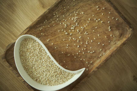 White sesame sesame seeds on a white plate. Wooden table. Soft selective blurred background.の写真素材