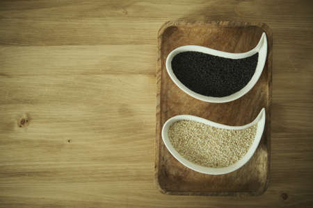 White sesame and black sesame seeds on a white plate. Wooden table. Soft selective blurred background.の写真素材