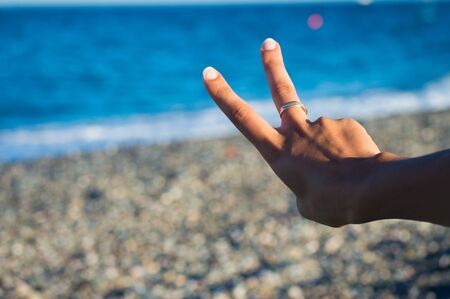 two fingers with sea in the background: it can be a sign of victory or number twoの写真素材