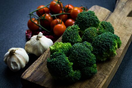 Broccoli, tomatoes and garlic, with cutting board and dark background