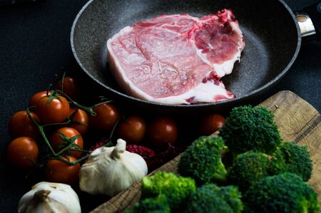 Meat in a pan to cook, topped with tomatoes, broccoli and garlic