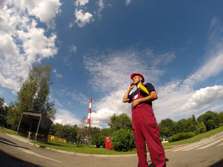 Industrial worker with cell phone against a blue sky with white clouds.