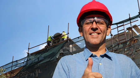 Construction engineer with two construction workers working on scaffolding in the background showing...