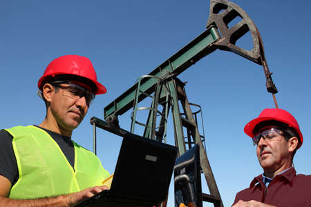 Engineers using laptop computers outdoors next to pump jack in the oil fieldの写真素材