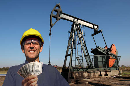 Oil worker or petroleum engineer holding US dollar bills in front of oil well. Best paid jobs conceptの写真素材