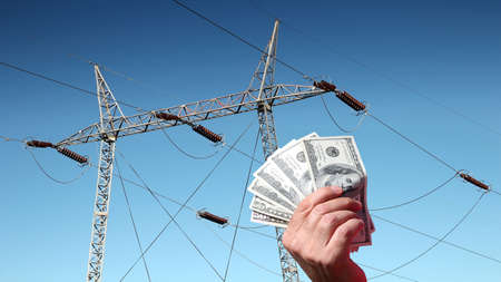 Hand holding US dollar bills in front of a high voltage power linesの写真素材