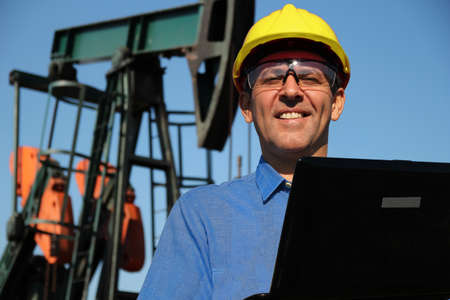 Petroleum engineer with laptop computer in an oilfield, monitoring work of the oil pump jack. Petroleum engineer using laptop outdoors, develop methods for extracting oilの写真素材