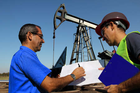 Petroleum engineers with laptop and blueprint in an oilfield manage the technical aspects related to exploration, drilling and oil productionの写真素材