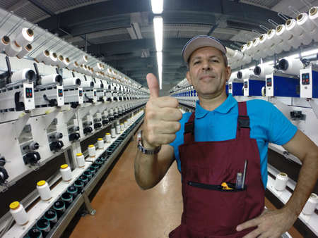 Industrial worker in textile factory during repair work showing thumbs upの写真素材