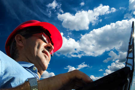 Close up low angle portrait of engineer using laptop outdoors with a bright blue sky backgroundの写真素材