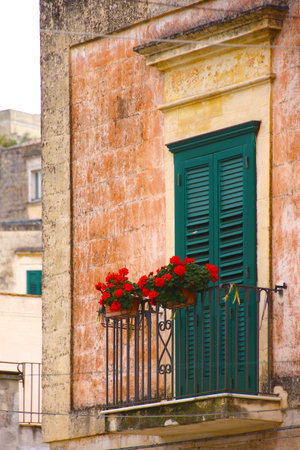 Typical Italian balcony with old windows and a colorful old wall. In it is a pot with very colorful red flowersの写真素材