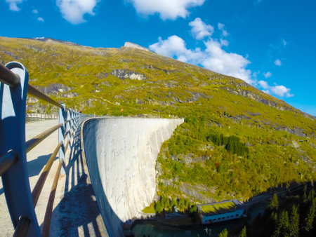 Image of a dam in the mountains, in the background the snowy peaks and a yellow forest. Swiss Alps, picturesque mountain landscape on a cloudy dayの写真素材