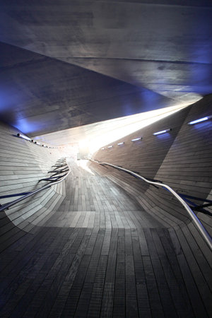 Organically shaped wooden ramp, in the background a bright flash. Dark image of a wavy path with a wooden texture and a faceted shape. Abstract conceptual image, representation of the path, journey, towards a brighter futureの写真素材