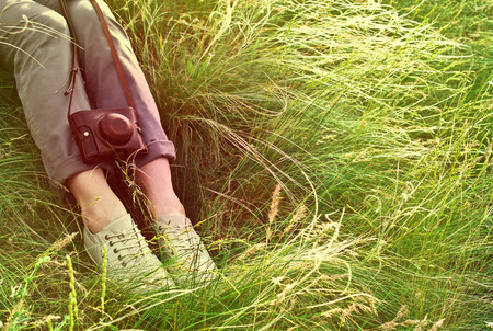 Feet woman and vintage retro photo camera outdoor. Girl sitting on the grassの写真素材