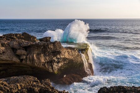 Wave crashing against cliff at Devil's Tear, Nusa Lembongan, Bali, Indonesia. Pool on top of cliff; ocean and sky In background.の写真素材