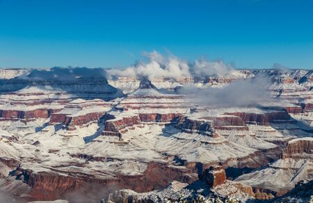 Grand Canyon in winter from the south rim. Covered in snow, clouds clinging to the top of the canyon. Blue sky above.の写真素材