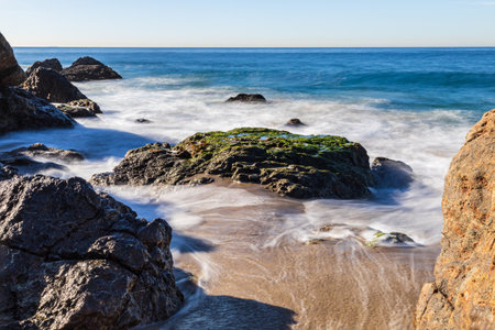 Rocky beach at Malibu, California. Waves receding from the sandy shore; blue Pacific Ocean in the background.の写真素材