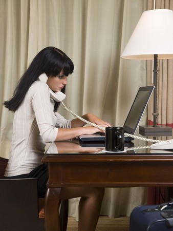 A businesswoman works late into the night on a laptop in her hotel room while on a business trip.の写真素材