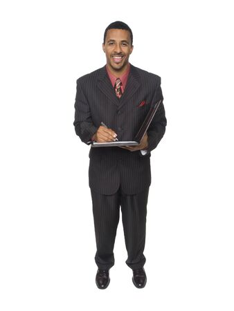 Isloated full length studio shot of an African American man looking at the camera while smiling and writing on his notepad.の写真素材