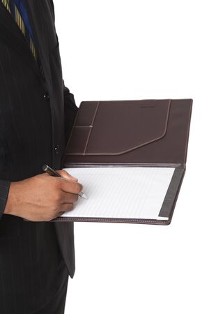 Isolated closeup studio shot of a businessman standing and writing in a notebook he is holding.の写真素材