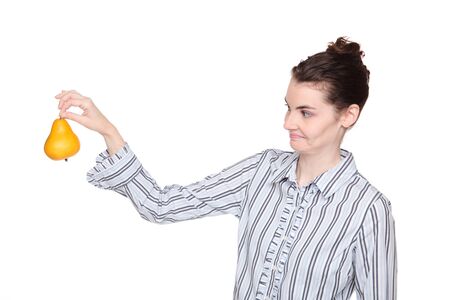 Isolated studio shot of a Caucasian woman holding out a pear at arms length with a disgusted expression.の写真素材