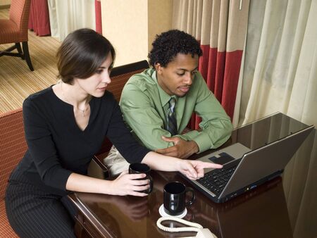 A team of businesspeople review results on a laptop while working late in a hotel room on a business trip.の写真素材