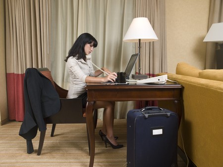 A businesswoman works late into the night on a laptop in her hotel room while on a business trip.の写真素材