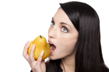 Isolated studio shot of a dark haired caucasian woman looking happily at a vibrant fresh pear.の写真素材