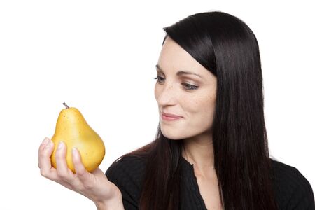Isolated studio shot of a dark haired caucasian woman looking happily at a vibrant fresh pear.の写真素材
