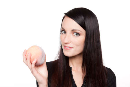Isolated studio shot of a dark haired caucasian woman looking happily at a fresh peach.の写真素材