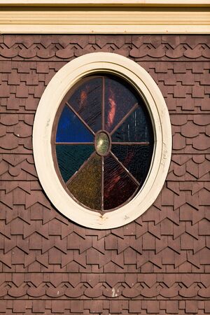 An old stained glass window on a New England gingerbread cottage with wood tile accents.の写真素材