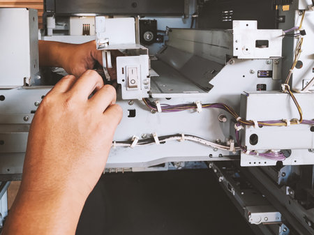 A technician repairs a photocopier by dismantling machine and examining wires connected to power button and circuit board to determine cause of malfunction.の写真素材