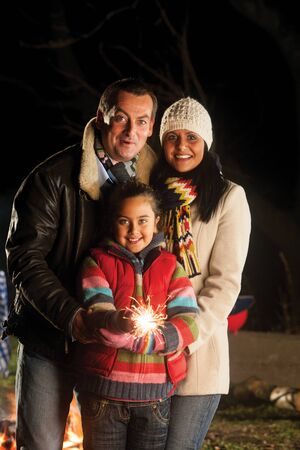 Young girl posing with a sparkler on bonfire night, with her parentsの写真素材