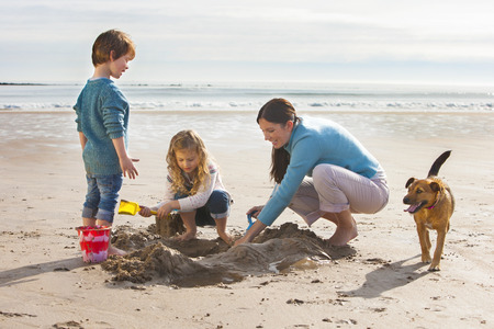 Mother playing on the beach with her son and daughter, with their dog accompanying them.の写真素材