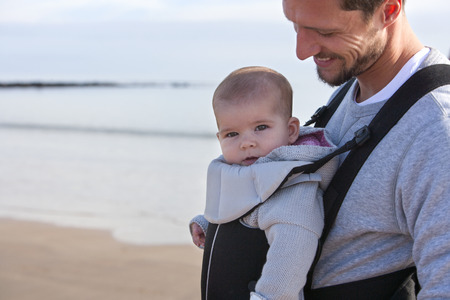 Father carrying his baby daughter on his chest along the beach.