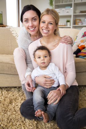 Female couple sit together with their son in their home and smile for the cameraの写真素材