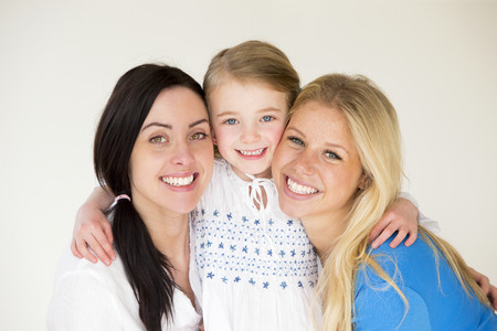Same sex female couple posing with their daughter in front of a plain backgroundの写真素材