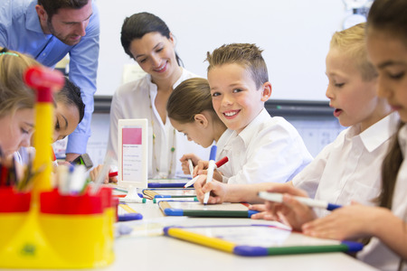 School boy smiles at the camera as he sits at his desk while working.の写真素材