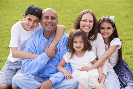 A portrait of a mixed ethnicity family, mum and dad have three cute children between the ages of 4 to 10. They are sitting down and smiling happily at the camera.の写真素材