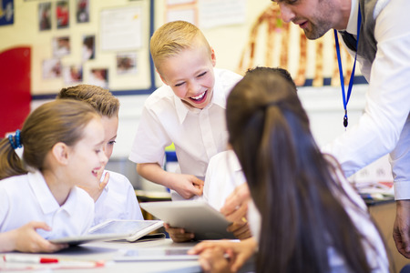 Happy students in classroom using a digital tablet, they are all wearing uniforms.の写真素材