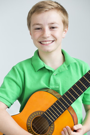 Portrait of a young boy posing for the camera with a guitar. He is standing in front of a plain backgroundの写真素材