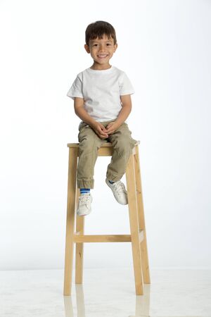 Cute young boy sitting on a stool against a white background, smiling for the camera.の写真素材