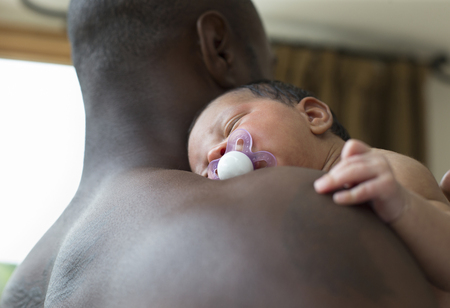 A close up of a newborn baby girl sleeping on her fathers shoulder.の写真素材