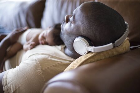 A father and newborn baby daughter at home sleeping. He is wearing headphones and wearing casual clothing.の写真素材