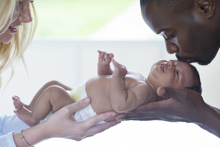 Mother and Father holding their new born multi ethnic baby. The mother is smiling and the father is...