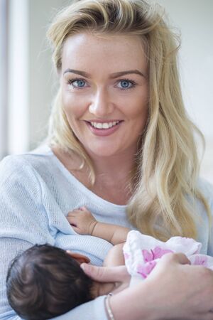 A portrait of a mother holding her newborn daughter. She is smiling at the camera.の写真素材