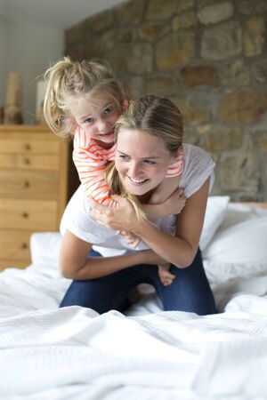 Mother and daughter playing on a bed at homeの写真素材