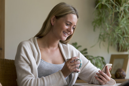 Woman sitting at a table in her home using a smartphoneの写真素材